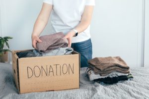 Donation concept. Young woman in white t-shirt with donation box at home. Woman donates clothes